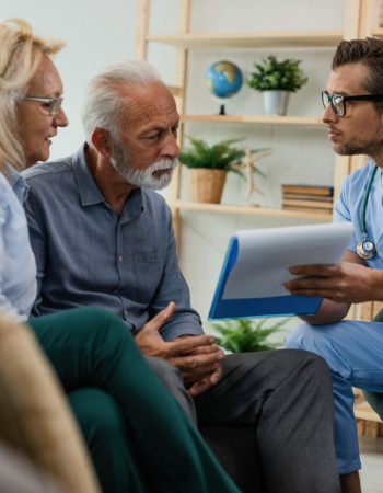 General practitioner showing to senior couple medical documents while being in home visit.